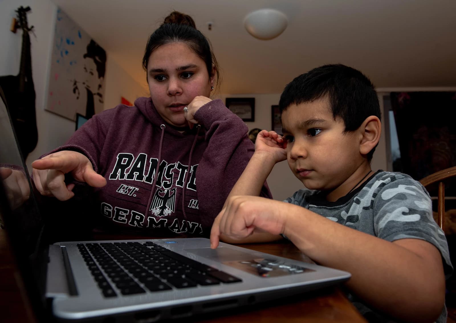 Woman pointing at a laptop screen while a child uses the trackpad.