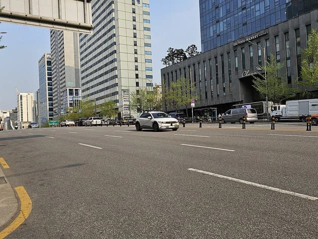 White Hyundai IONIQ 5 NE1 RoboTaxi driving on a multi-lane city street.
