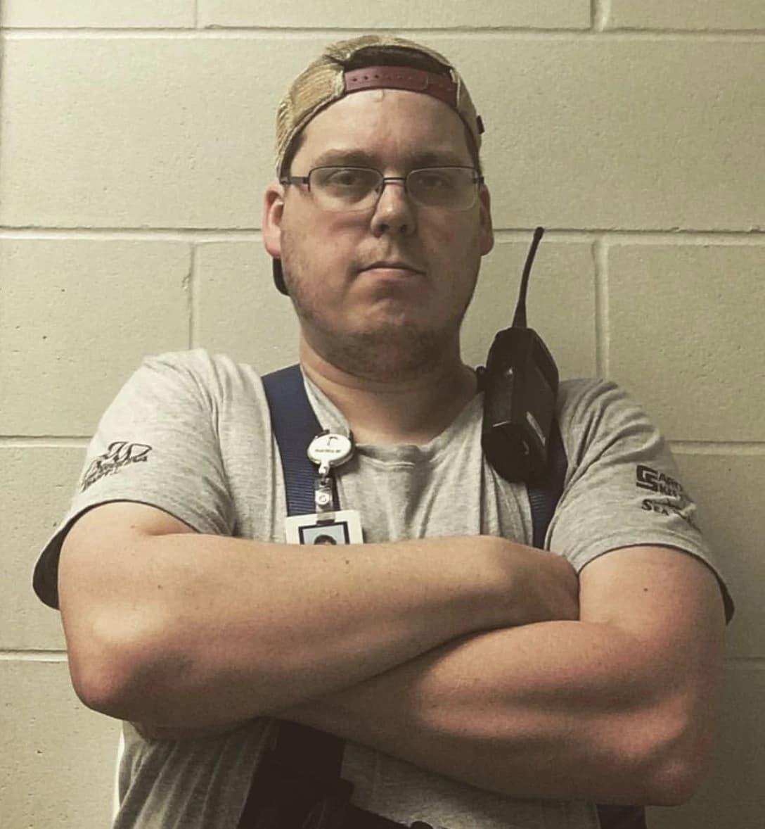 Warehouse worker wearing a cap and holding a radio with arms crossed.
