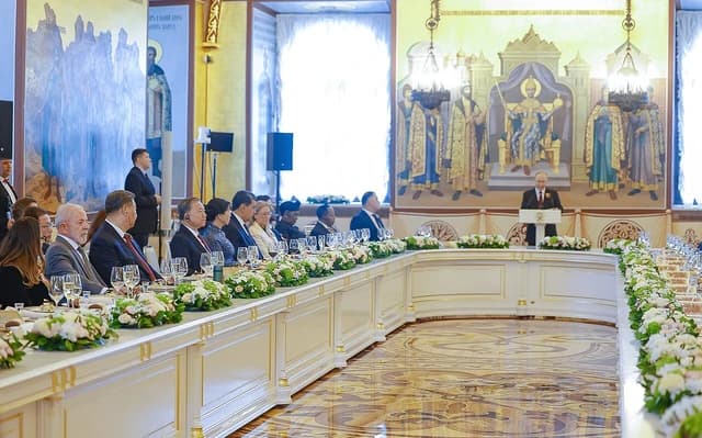 Vladimir Putin speaking at a podium while world leaders sit at a long table.
