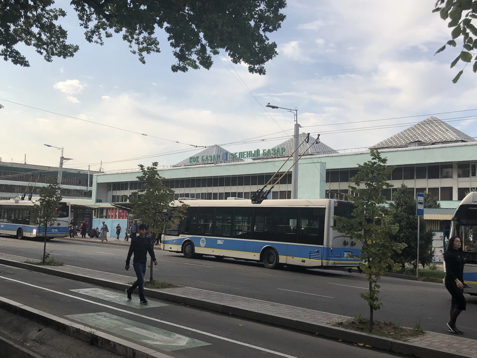 Exterior view of the Green Bazaar market building in Almaty with trolleybuses and people.