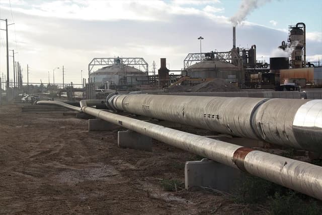 Industrial geothermal power plant with large insulated pipes in the foreground and steaming facilities in the background.