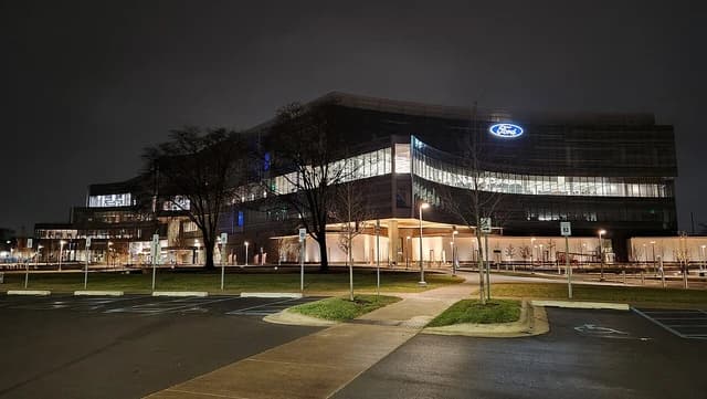 Ford World Headquarters building illuminated at night, viewed from an adjacent parking lot.