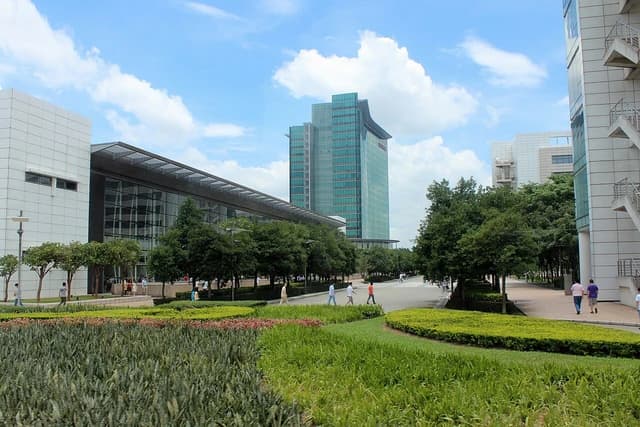 Huawei Headquarters campus buildings, green landscaping, and pedestrian walkways under a blue sky.