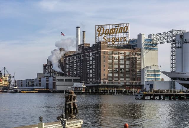 Domino Sugar refinery building with large sign and smokestacks releasing steam.