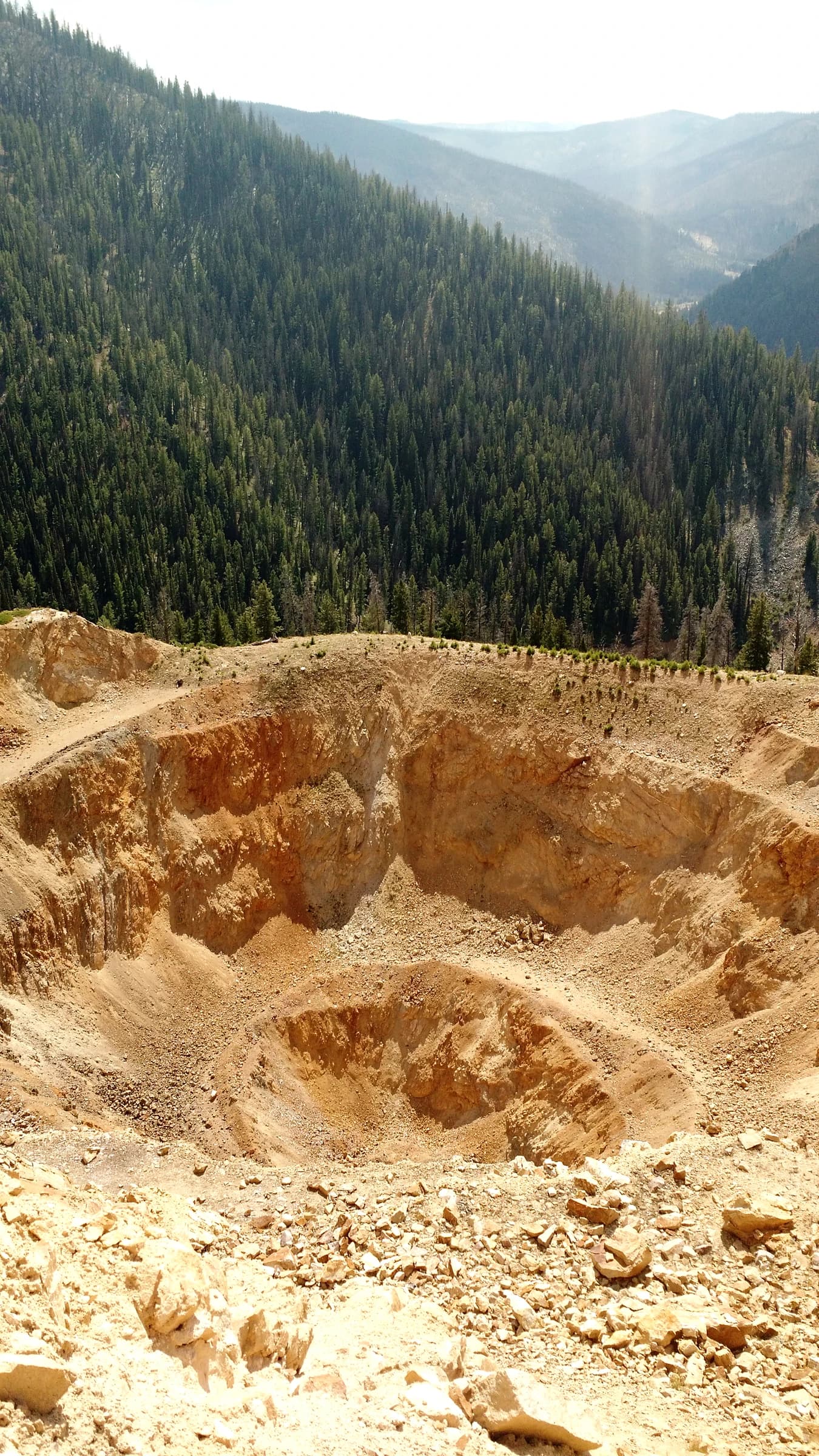Open-pit mine within the Stibnite Mining District, showing excavated earth and distant mountains.