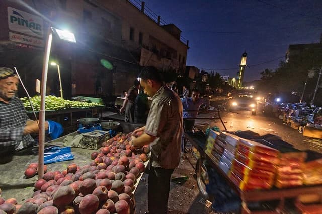Vendors at a night market in Sulaymaniyah, Kurdistan, selling fruit under streetlights.