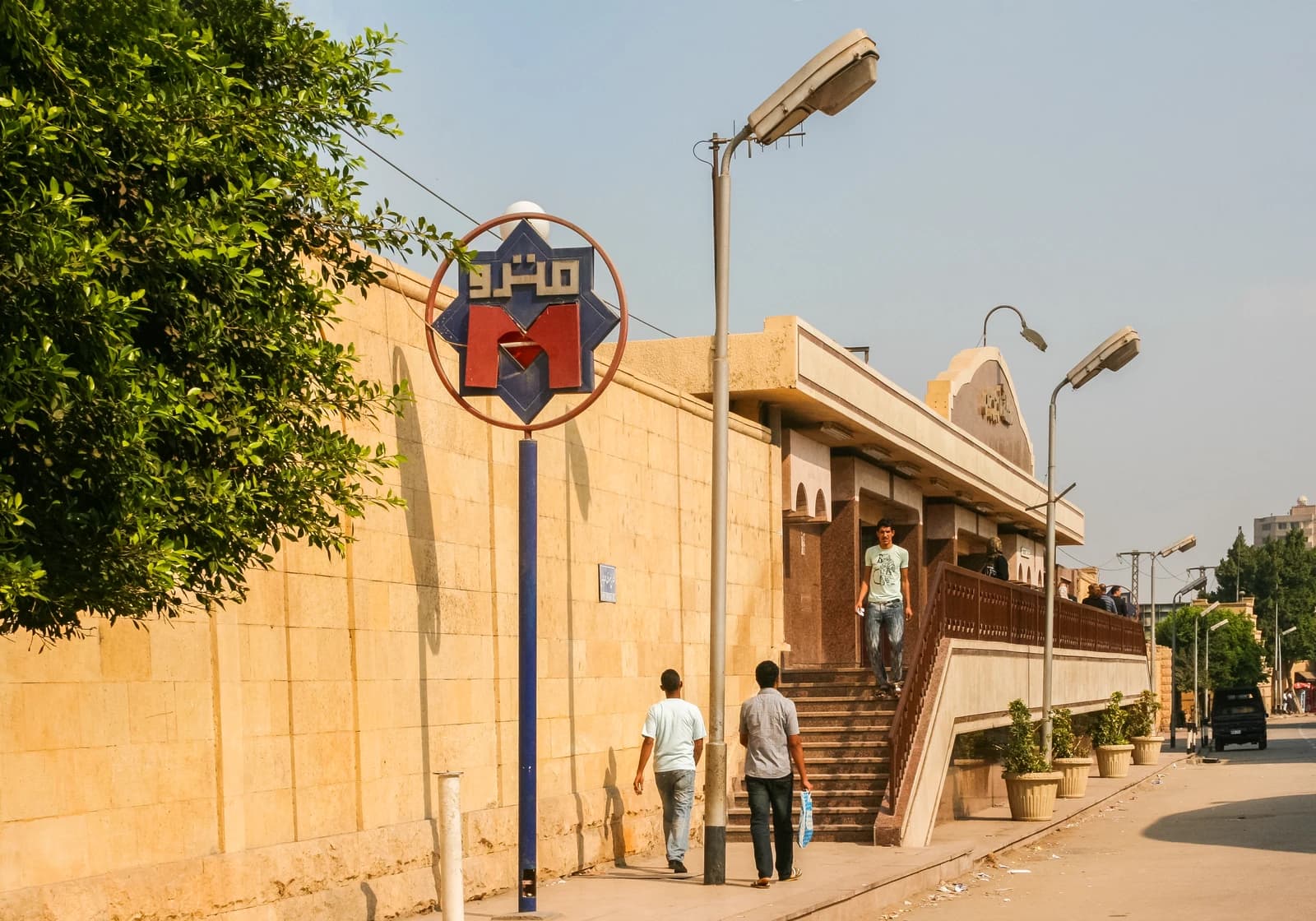 People walk on a sidewalk outside a Cairo Metro station building in Old Cairo, Egypt.