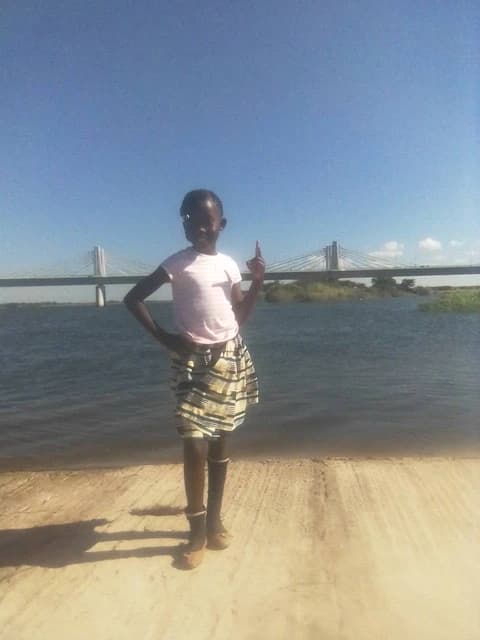 Young Zambian girl stands by the Zambezi River with the Kazungula Bridge visible behind her.