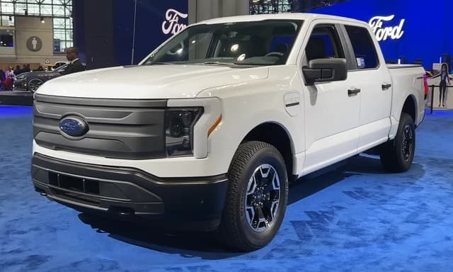 A white 2023 Ford F-150 Lightning Pro electric pickup truck is displayed at an event.