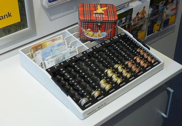 Euro banknotes and coins organized in a black cash register insert, next to a red Felix the Rabbit tin.