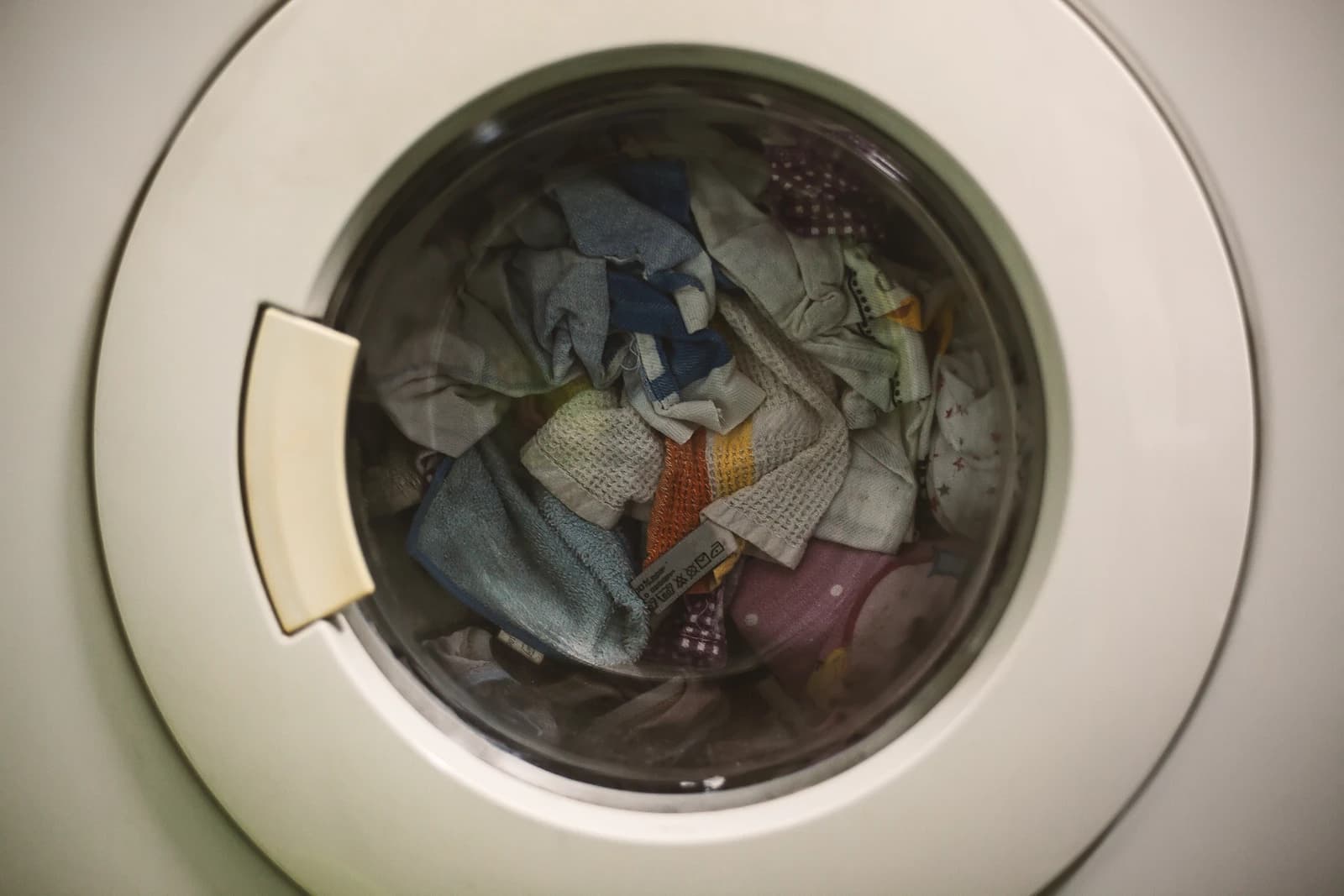 Close-up of a washing machine's circular door with various colorful clothes inside.