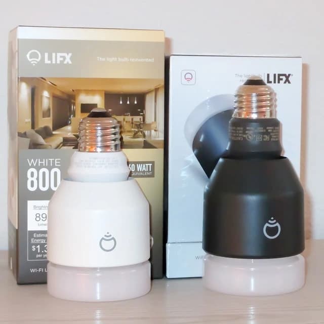 LIFX smart light bulbs, one white and one black, standing next to their product boxes.