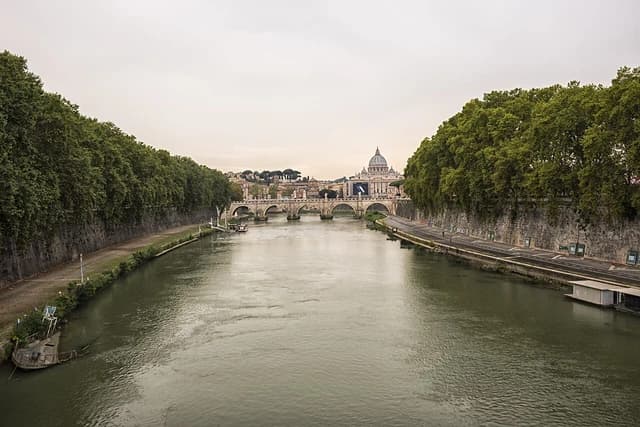 Tiber River in Rome with a bridge and St. Peter's Basilica dome visible in the distance.