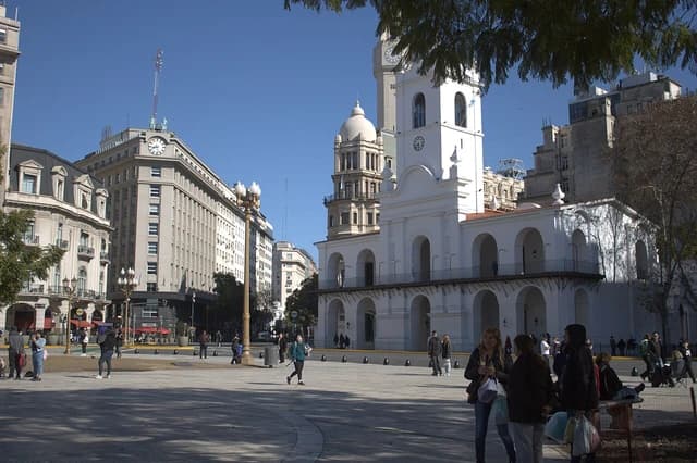 People walking in a plaza with historic buildings under a clear sky in Buenos Aires.