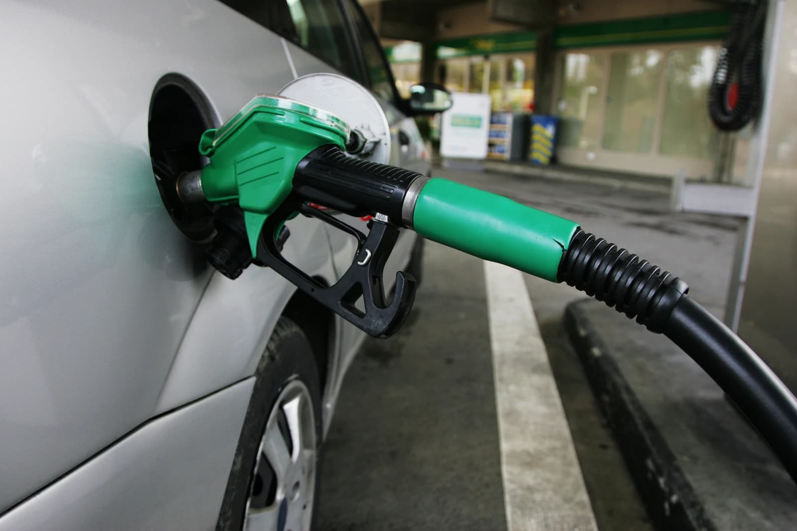Green fuel pump nozzle inserted into the fuel tank of a silver car.