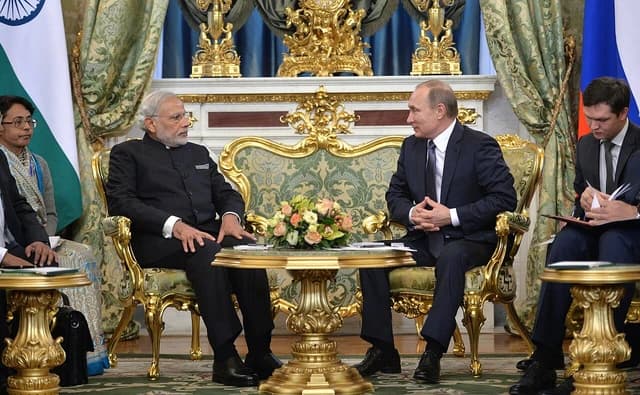 Vladimir Putin and Narendra Modi sitting in ornate chairs during a meeting.