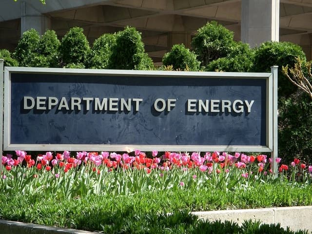 Department of Energy sign with flowers and shrubbery in front of a building.