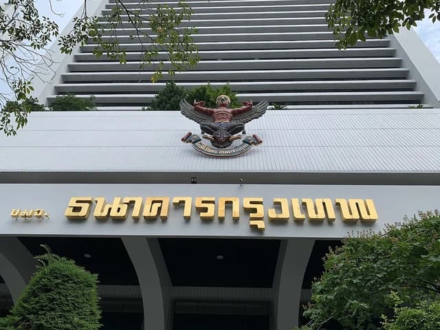 Exterior of Bangkok Bank head office building with Thai script and emblem.