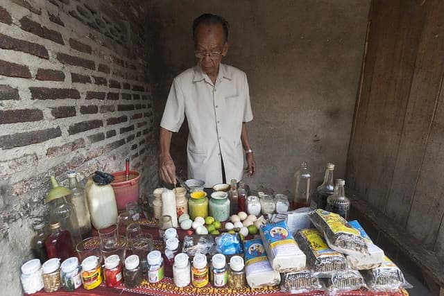 An older man stands behind a table displaying various traditional herbal remedies.