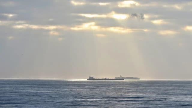 Oil tanker on the horizon, with sun rays breaking through clouds overhead.