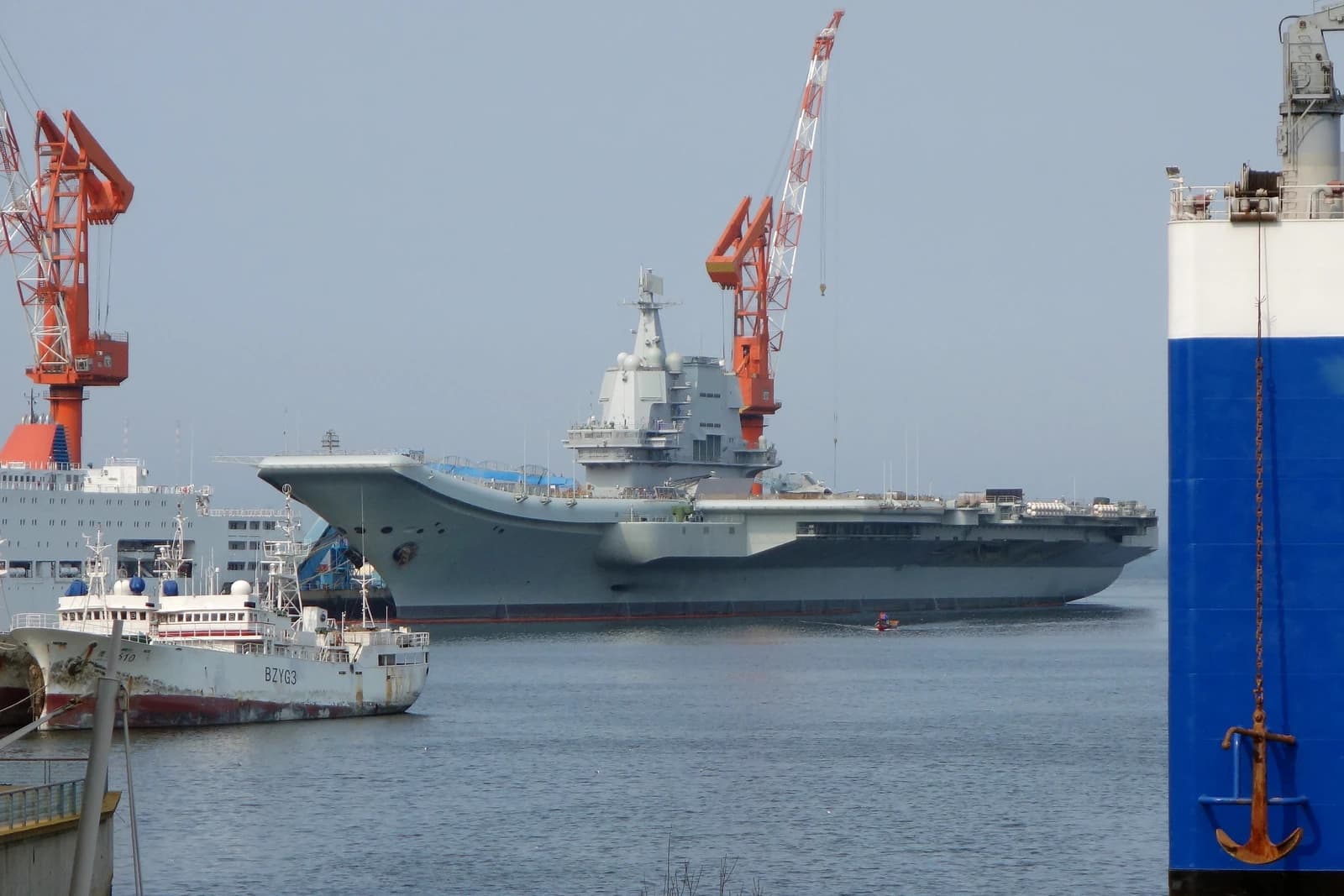 Chinese Type 002 aircraft carrier docked in a port with large cranes.