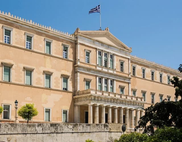 Main facade of the Building of the Parliament of Greece with a Greek flag flying above.