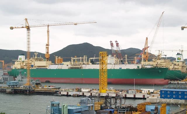 LNG carrier ship being constructed or repaired at a shipyard with industrial cranes.