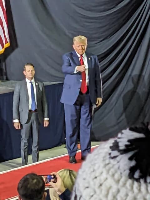 Donald Trump walking on stage at a rally, a security detail behind him.