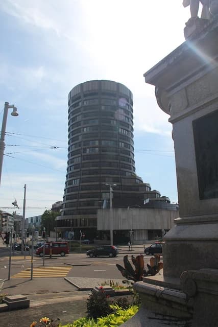 The circular, multi-story Bank for International Settlements building seen from a street with traffic.