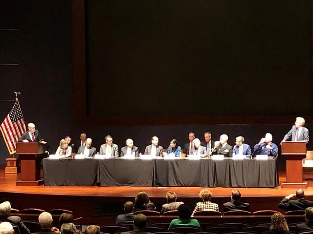 Government officials seated at a long table, with speakers at podiums on either side.