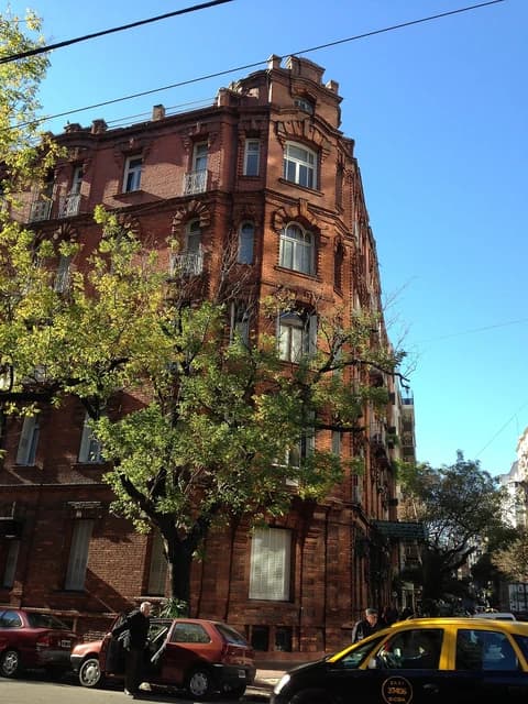 Brick building with arched windows on a street corner, trees, and parked cars.