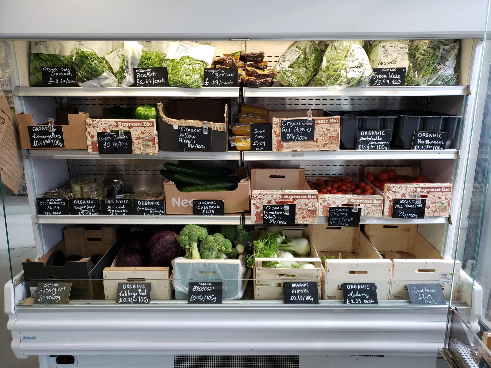 Organic produce including spinach, peppers, tomatoes, and broccoli displayed in a supermarket.