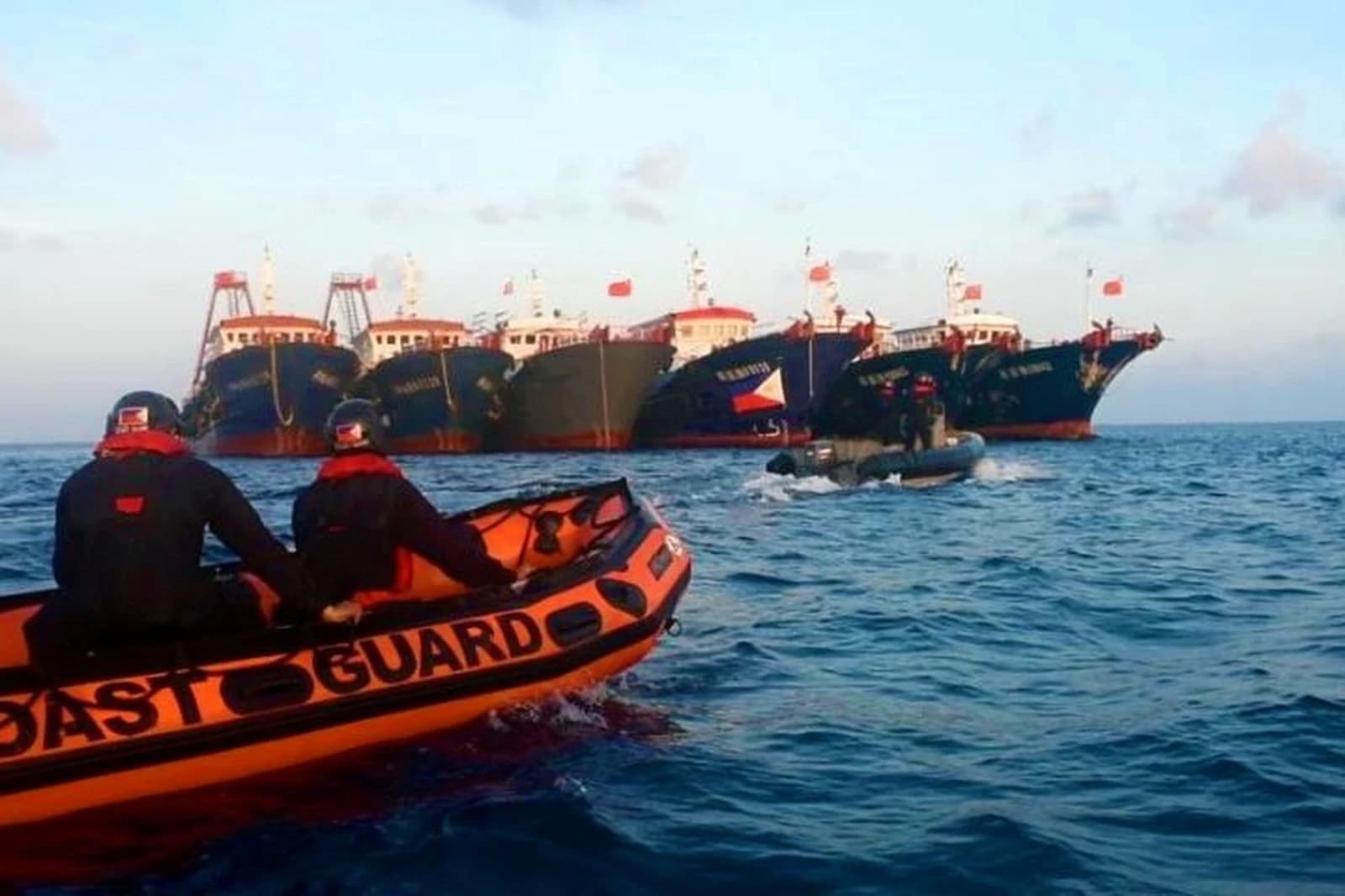 Filipino Coast Guard personnel in an orange boat observing multiple large Chinese ships.