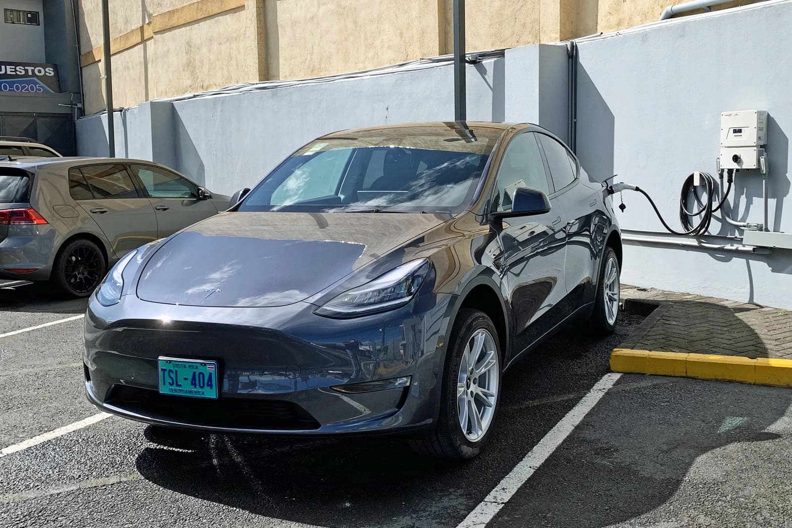 Gray Tesla Model Y car plugged into a charging station in a parking lot.