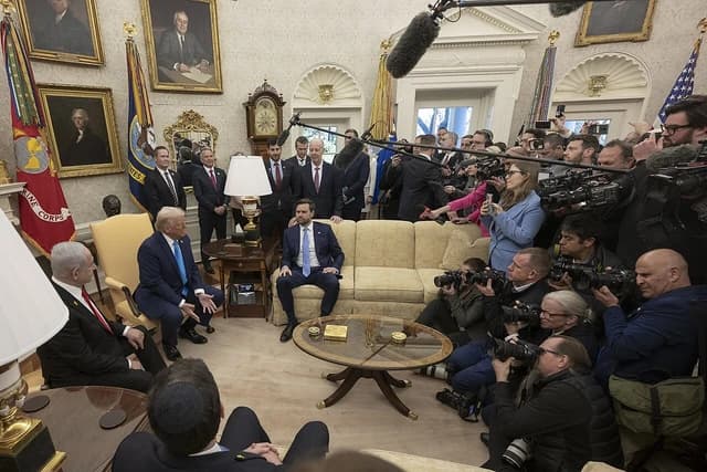 Donald Trump and Benjamin Netanyahu seated, talking, in the White House with press looking on.