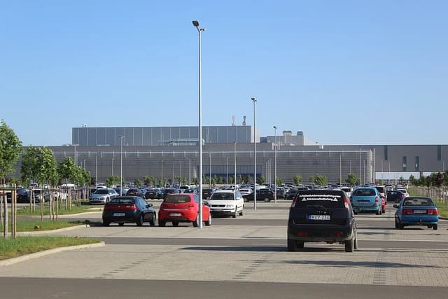Parking lot filled with cars in front of the BMW Debrecen factory building.