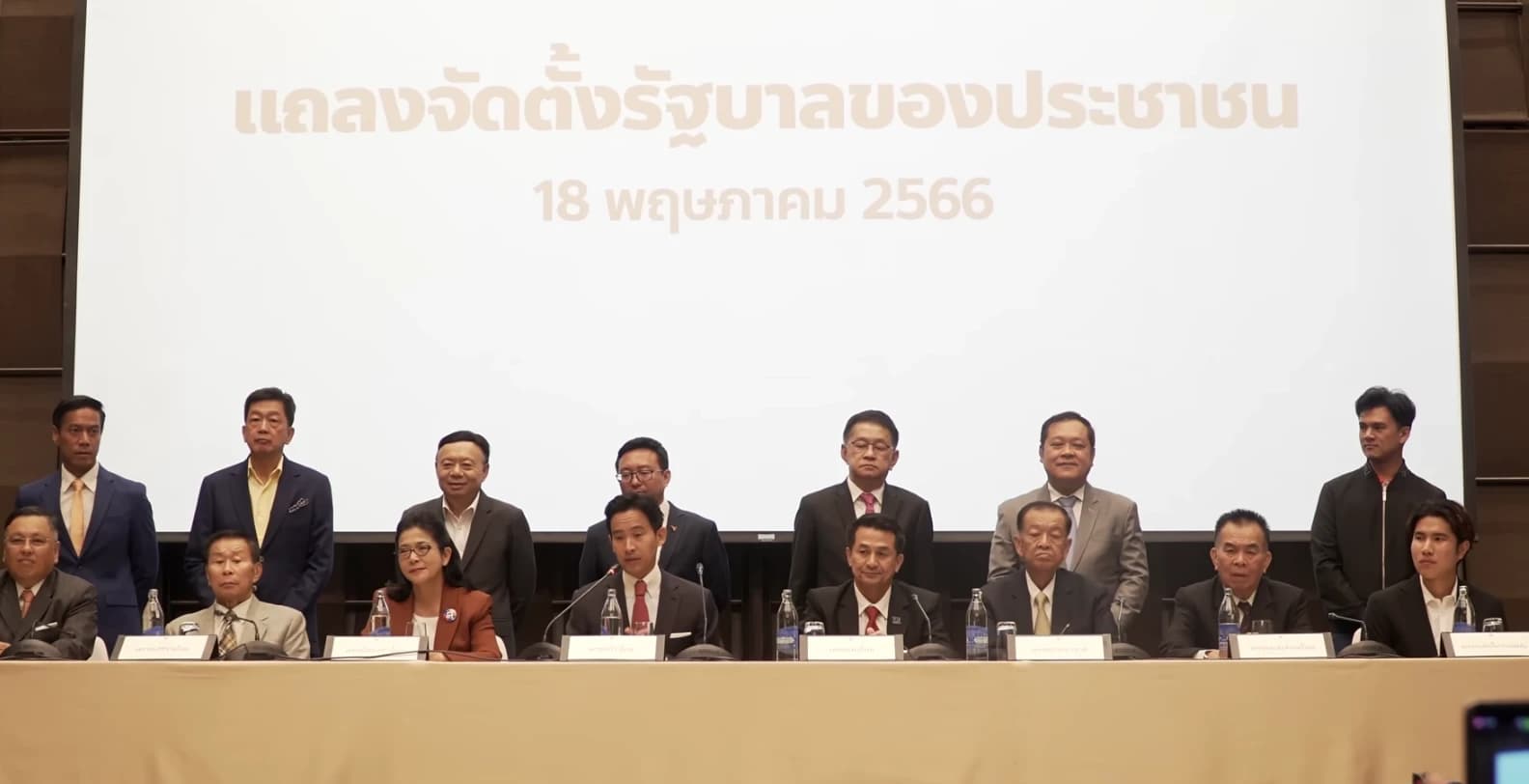 Thai politicians gathered at a press conference, some seated, others standing.