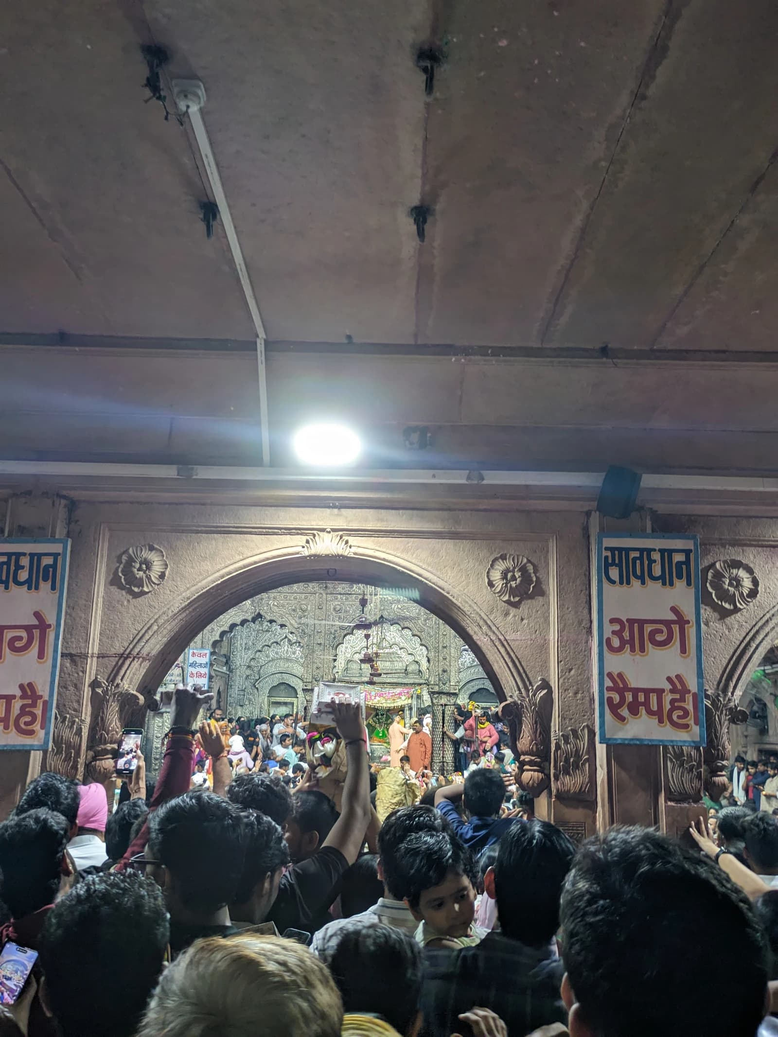 A large crowd of people gathered inside a temple with intricate archways and carvings.