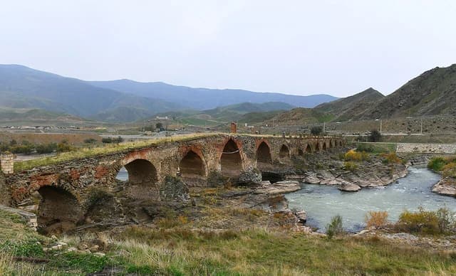 Ancient Khudaferin Bridge over a river, surrounded by mountains and hills.