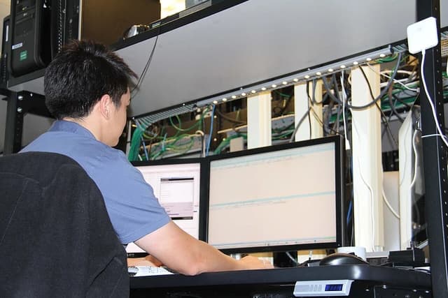 Technician monitoring multiple computer screens in a server room or data center.