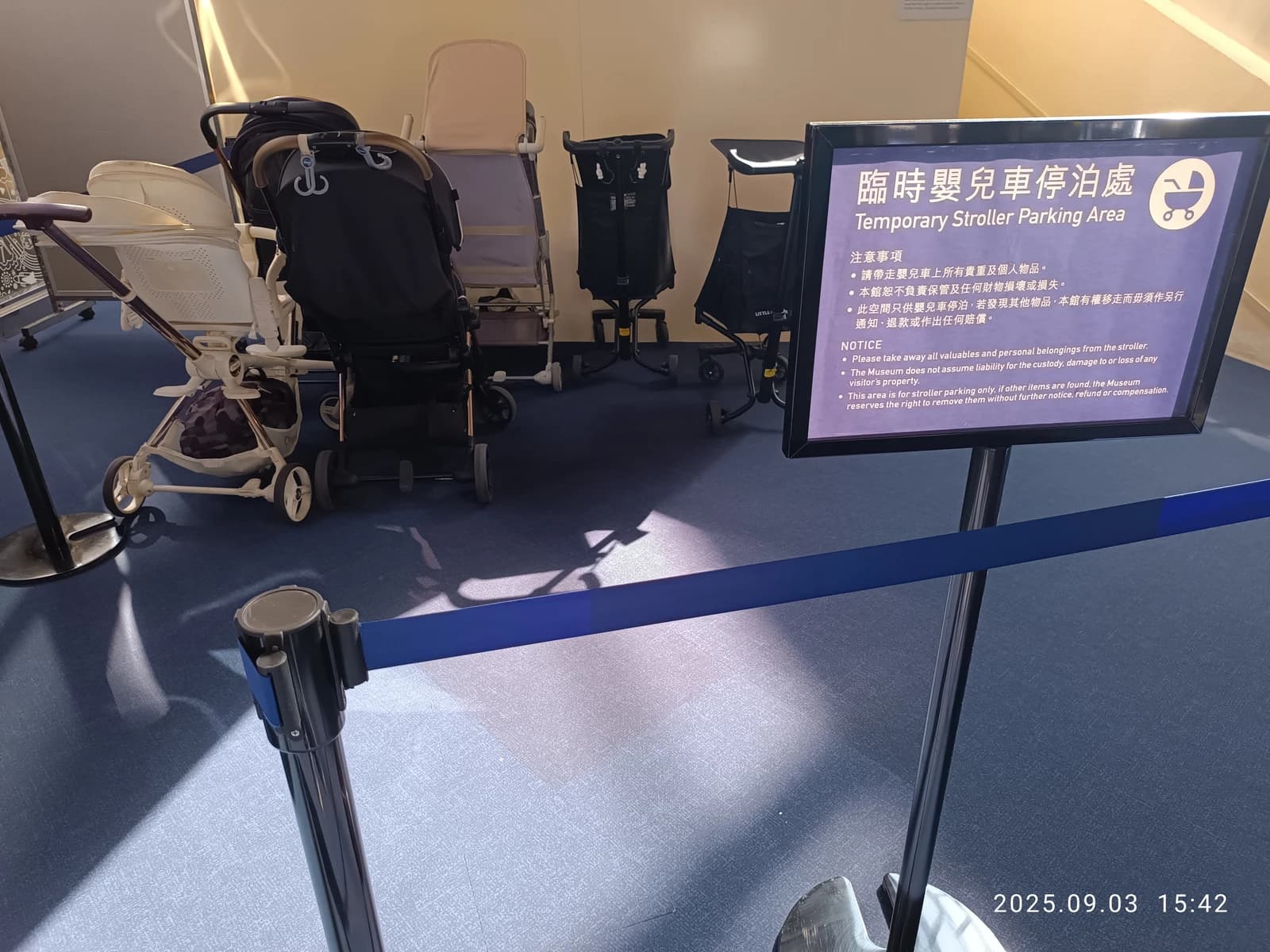 Temporary stroller parking area sign next to several parked baby strollers inside a building.
