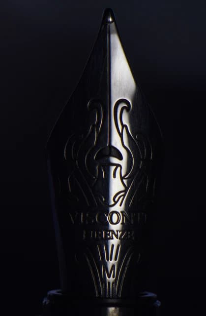 Close-up view of a silver fountain pen nib, illuminated by a strip of light.