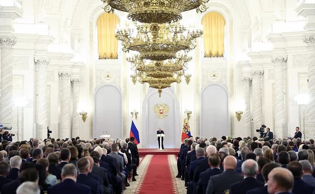 Russian President Vladimir Putin speaking at a podium to a seated audience.