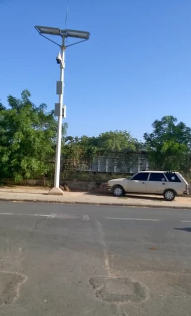 Surveillance camera mounted high on a street light post next to a public road.