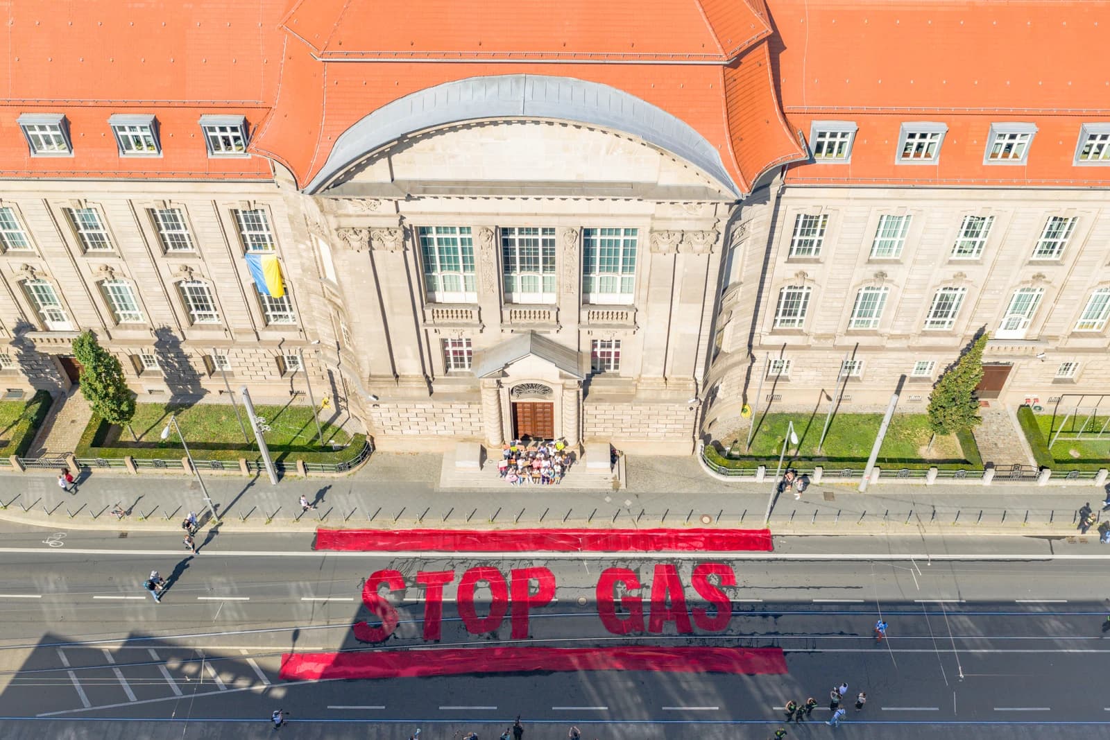 Aerial view of a protest 'Stop Gas' banner on a street in front of a large building.