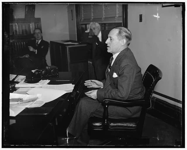 Marriner Eccles, Chairman of the Federal Reserve Board, sitting at a desk during a press conference.