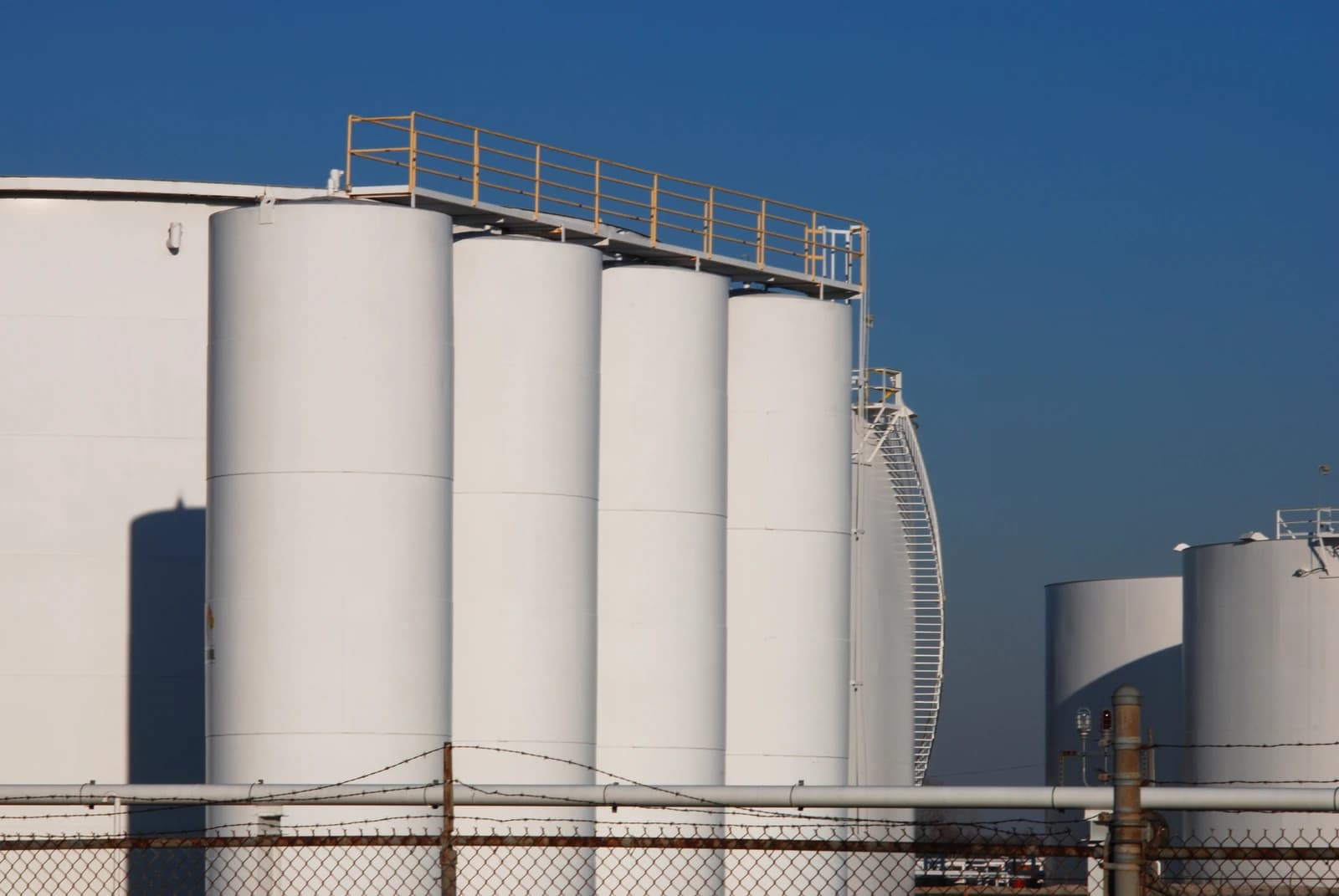 Several large white oil refinery storage tanks against a clear blue sky.