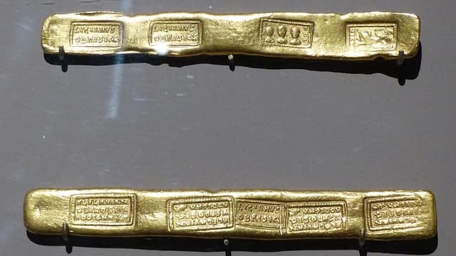 Two antique gold ingots displayed on a dark background.