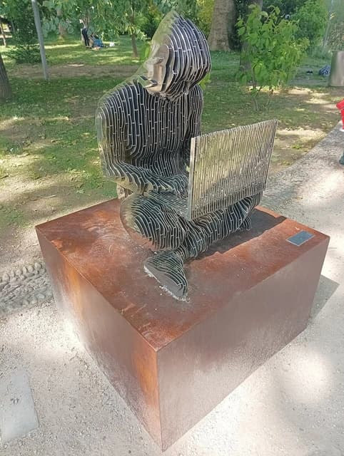 Statue of Satoshi Nakamoto sitting, looking at a laptop computer.